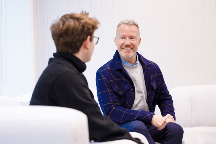 Two male colleagues are sat talking on a white sofa.
