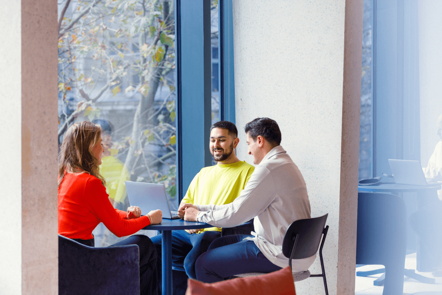A group of three graduates working together at a table by the window.