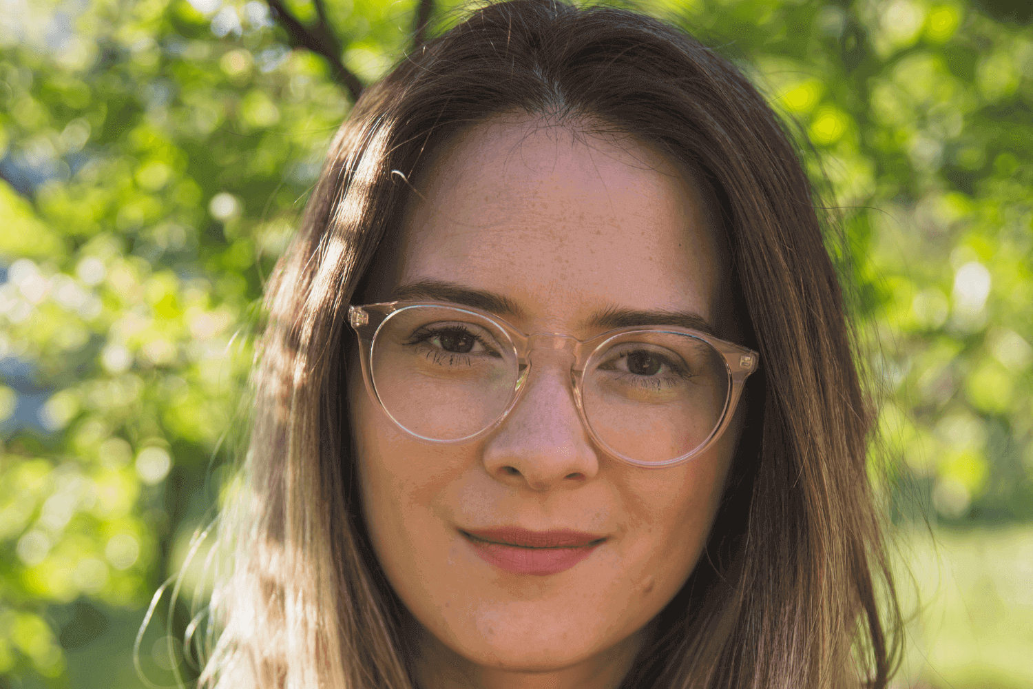 A woman wearing a black polo, with long light brown hair and glasses. She is outdoors.