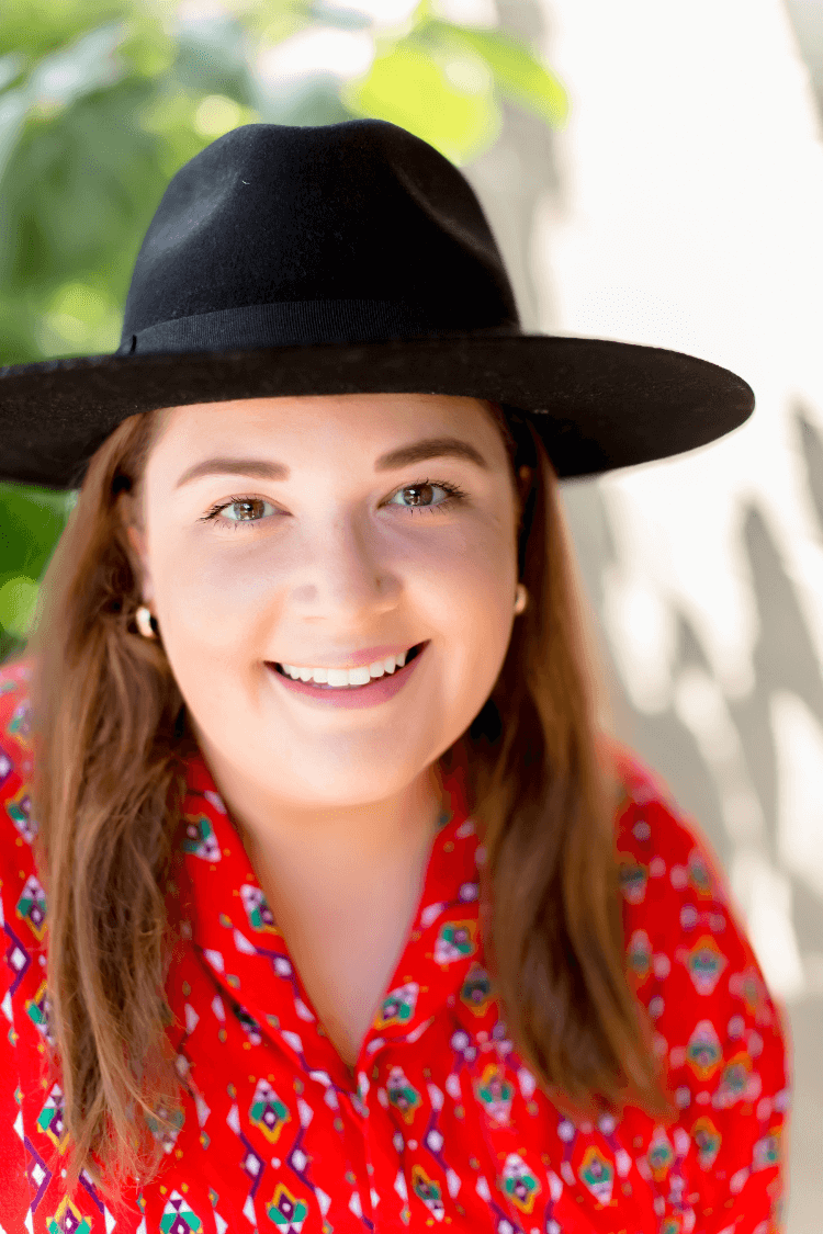 A woman in a red patterned shirt, and wearing a black wide brimmed hat. 