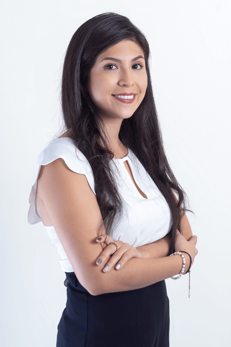 A woman with long dark brown hair. Her arms are folded and she wears a white short sleeved top. 