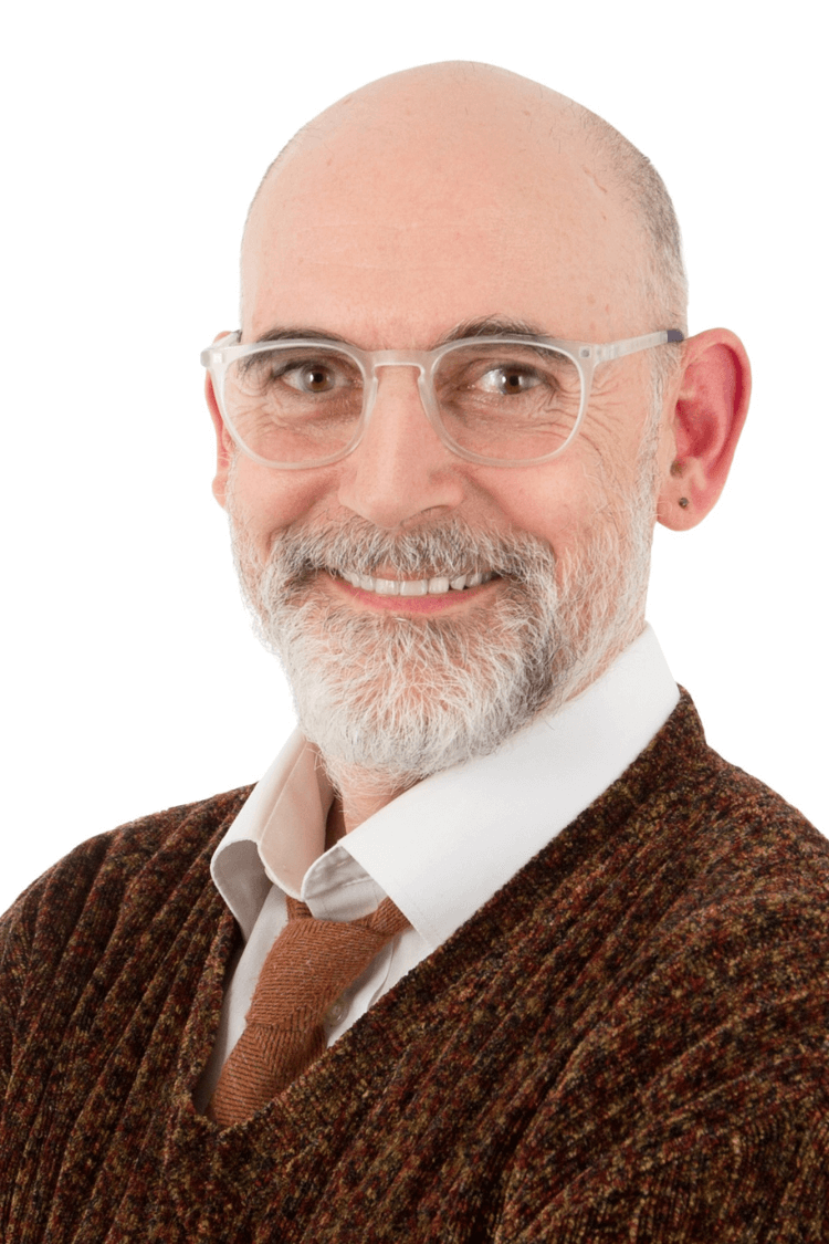 A gentleman with a beard and glasses. He is wearing a brown jumper, white shirt, and tie
