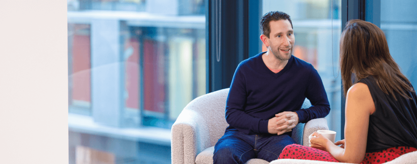 Ein Mann unterhält sich mit einer Kollegin, während er auf bequemen Stühlen sitzt. 