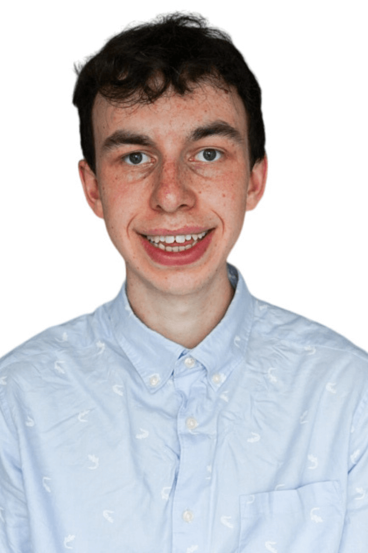 Ein junger Mann mit kurzen lockigen Haaren. Er trägt ein zugeknöpftes blaues Hemd. 