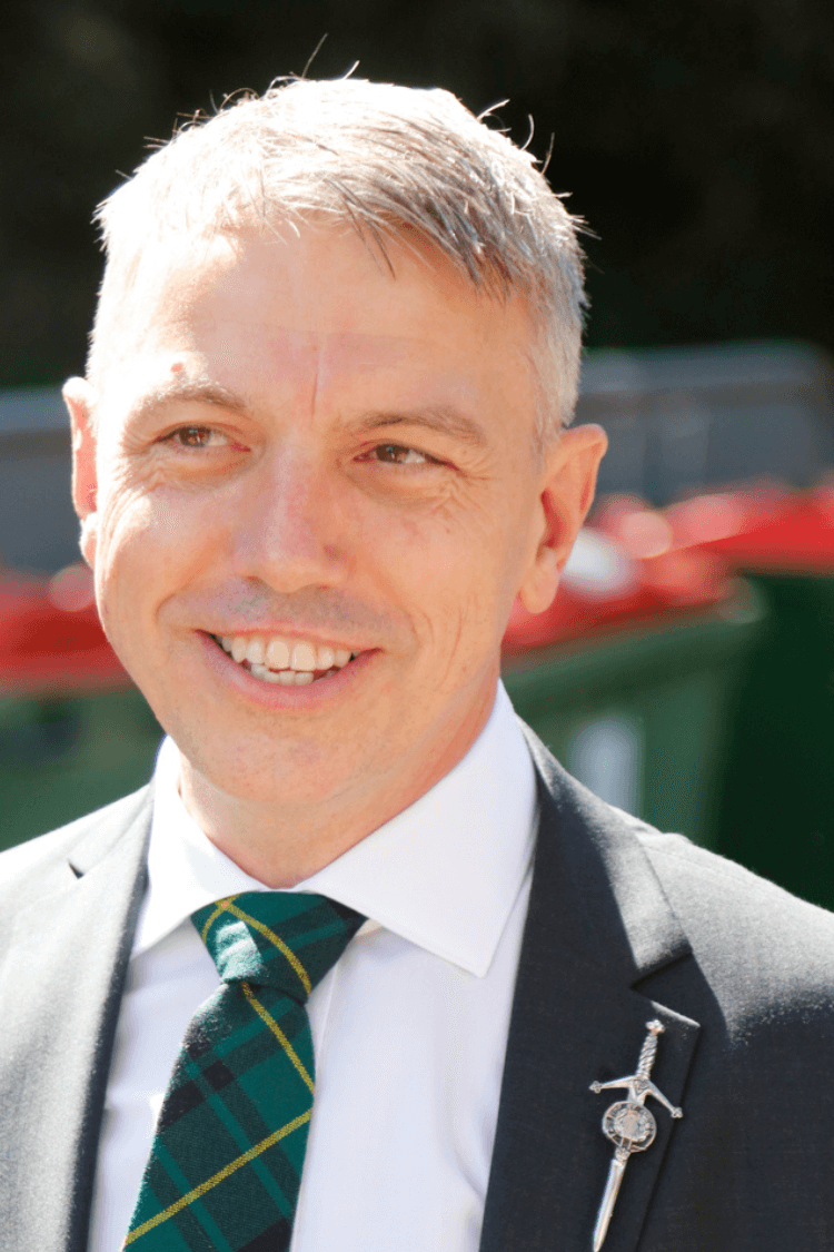 Un hombre con pantalón corto blanco, chaqueta negra y corbata verde. 