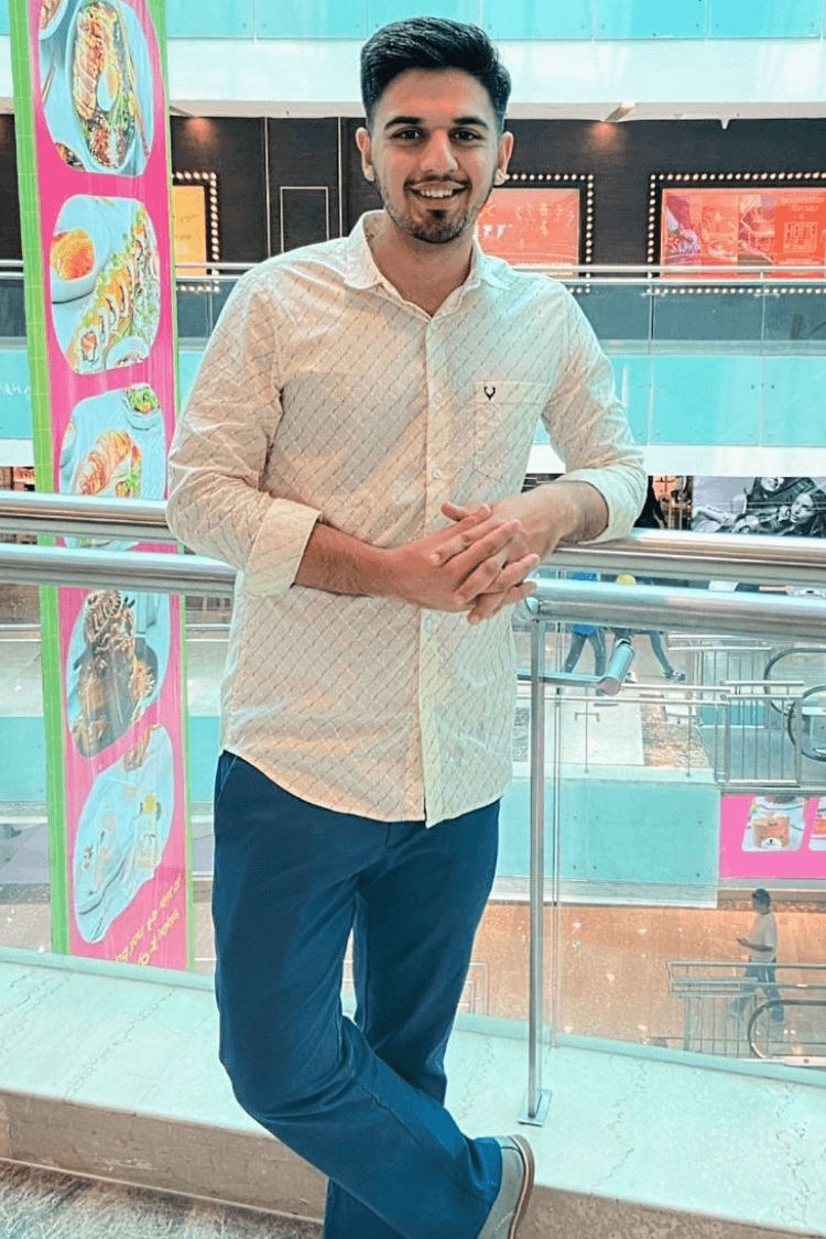 Un hombre con camisa blanca y vaqueros, apoyado en la barandilla de un balcón de un centro comercial. 