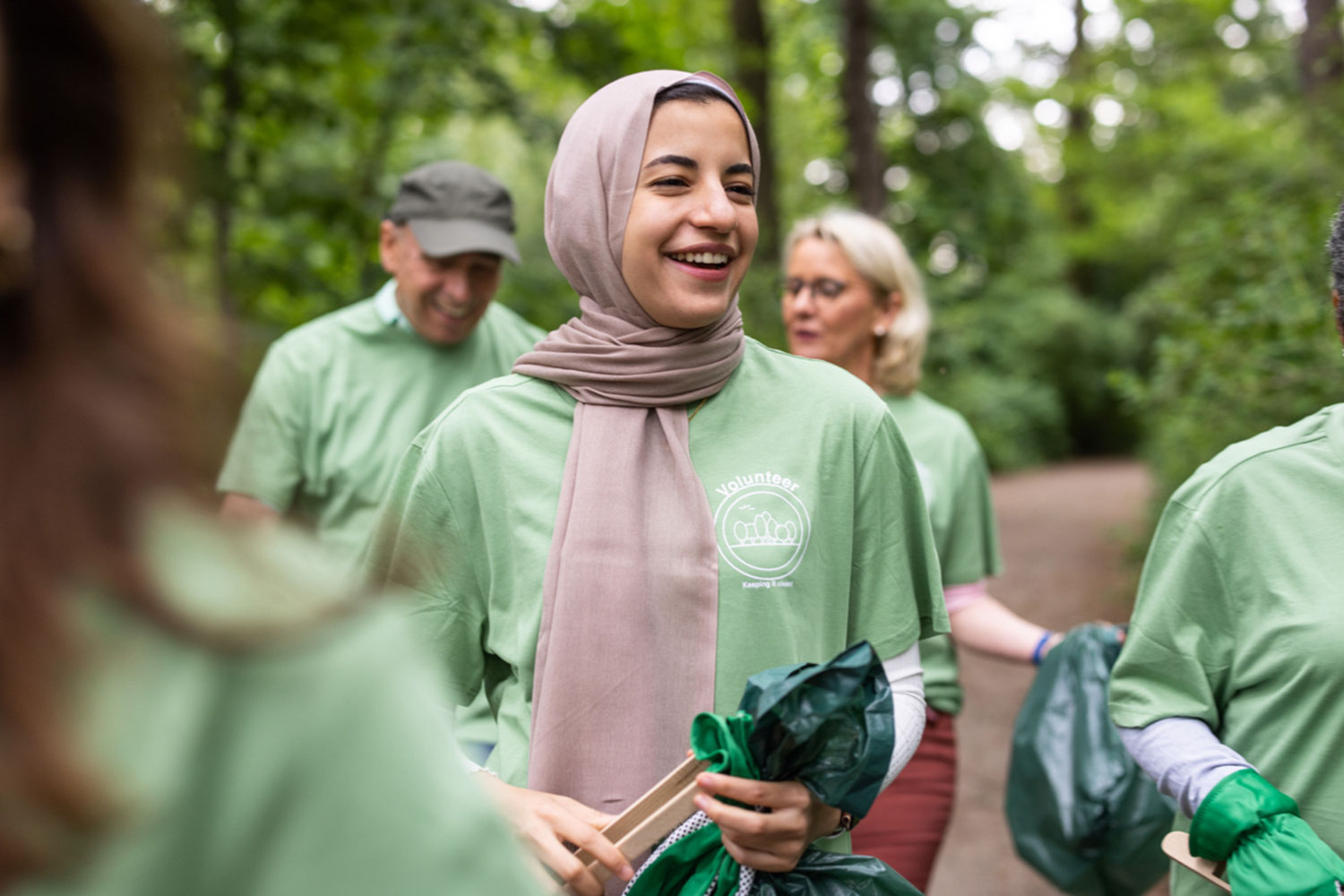 Une femme portant un foulard, un T-shirt vert et un sac à ordu
