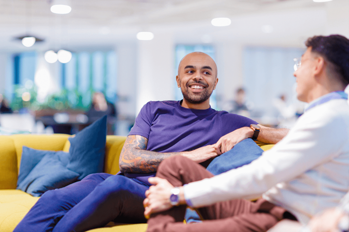 Twee collega's loungen op een gele bank en maken samen een praatje.