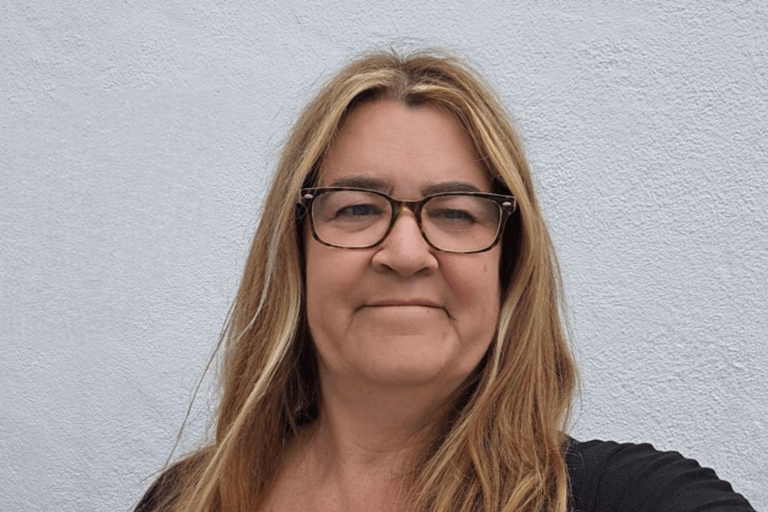 一位长发、戴眼镜的女士。她穿着一件黑色上衣。