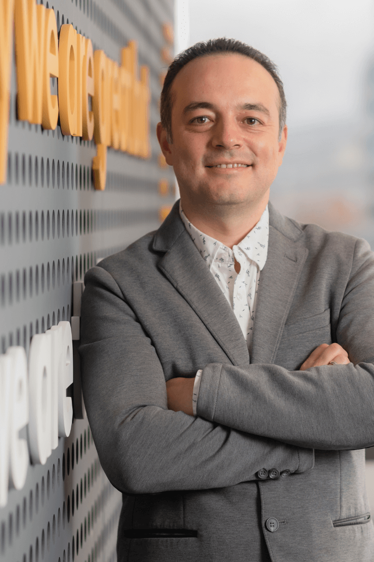 一名男子靠在墙上。他身穿灰色夹克，白色衬衫。